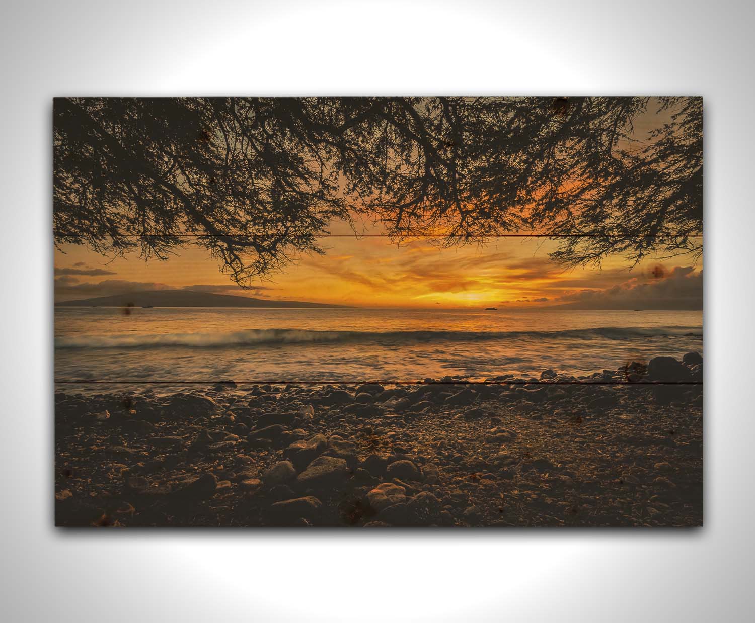 A photograph of the sunset over the ocean from Lāhainā in Maui, Hawaiʻi on a rocky beach, from underneath a tree. Printed on a wood pallet.