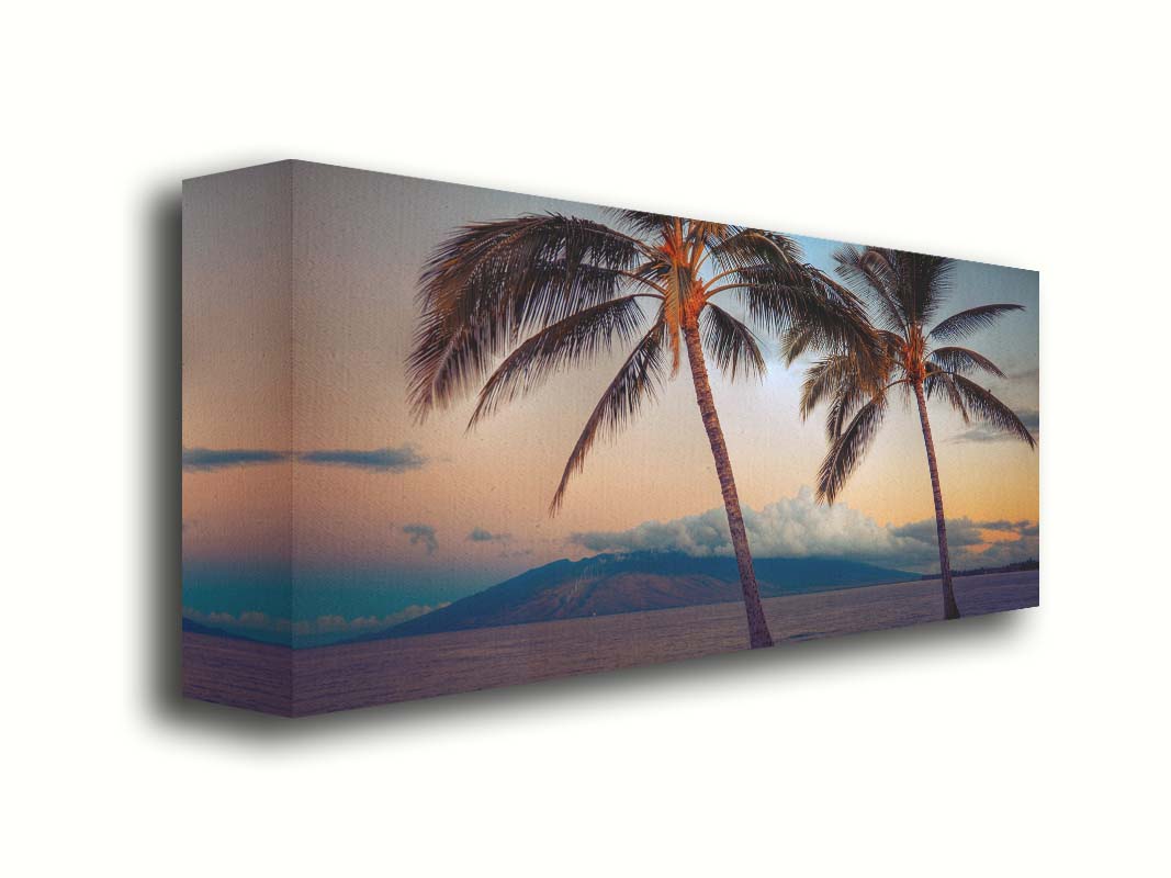 A photo of two palm trees in Maui at sunset, with the sea and cloud-topped mountains in the background. Printed on canvas.