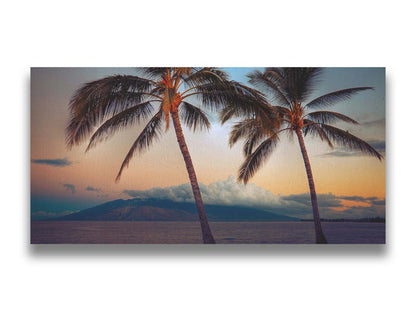 A photo of two palm trees in Maui at sunset, with the sea and cloud-topped mountains in the background. Printed on canvas.