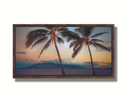 A photo of two palm trees in Maui at sunset, with the sea and cloud-topped mountains in the background. Printed on canvas in a float frame.