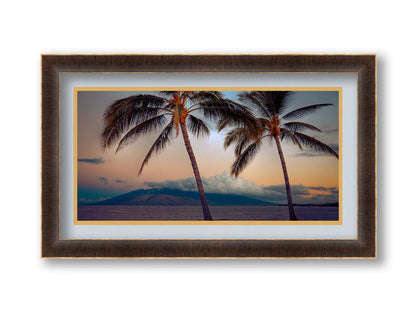 A photo of two palm trees in Maui at sunset, with the sea and cloud-topped mountains in the background. Printed on paper, matted, and framed.