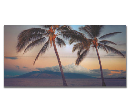 A photo of two palm trees in Maui at sunset, with the sea and cloud-topped mountains in the background. Printed on a box board.