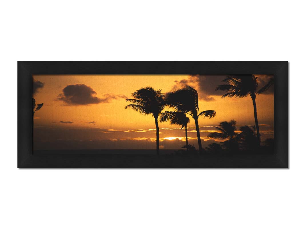 A photograph of an orange sunset over the sea, with striking palm trees silhouetted against the sky in Maui, Hawaiʻi. Printed on canvas and framed.