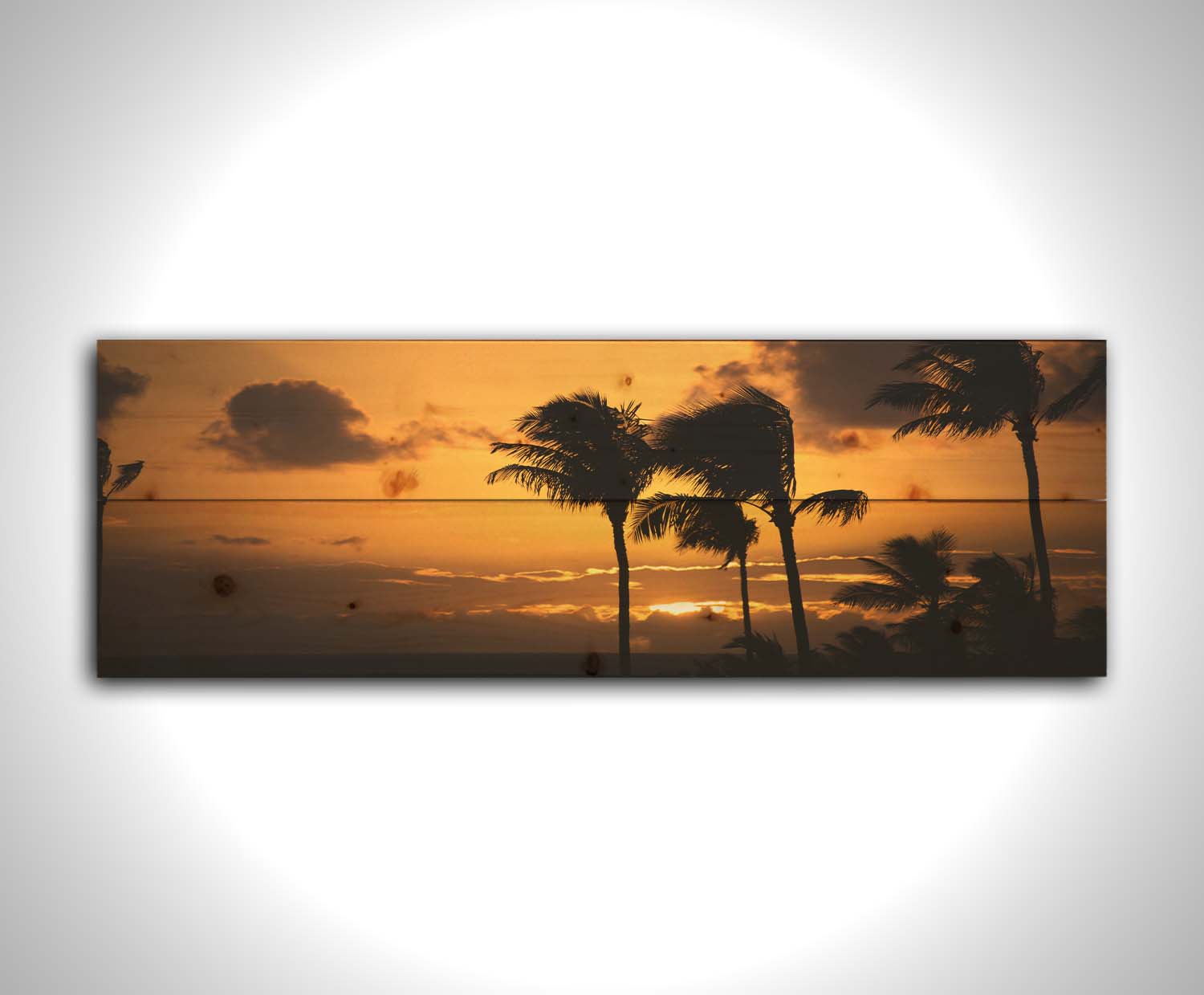 A photograph of an orange sunset over the sea, with striking palm trees silhouetted against the sky in Maui, Hawaiʻi. Printed on a wood pallet.