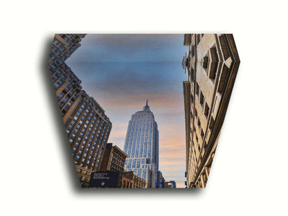 A photoraph looking up at the Empire State Building in New York against a blue sky and orange clouds. Printed on canvas.