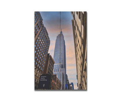 A photoraph looking up at the Empire State Building in New York against a blue sky and orange clouds. Printed on a box board.