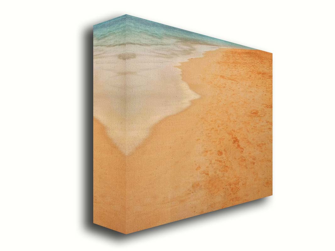 A photograph of beach sand. The warm hues of golden sand are contrasted by the cool ocean water. Printed on canvas.