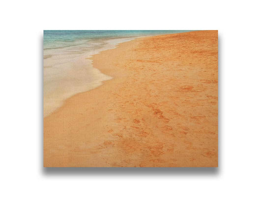 A photograph of beach sand. The warm hues of golden sand are contrasted by the cool ocean water. Printed on canvas.