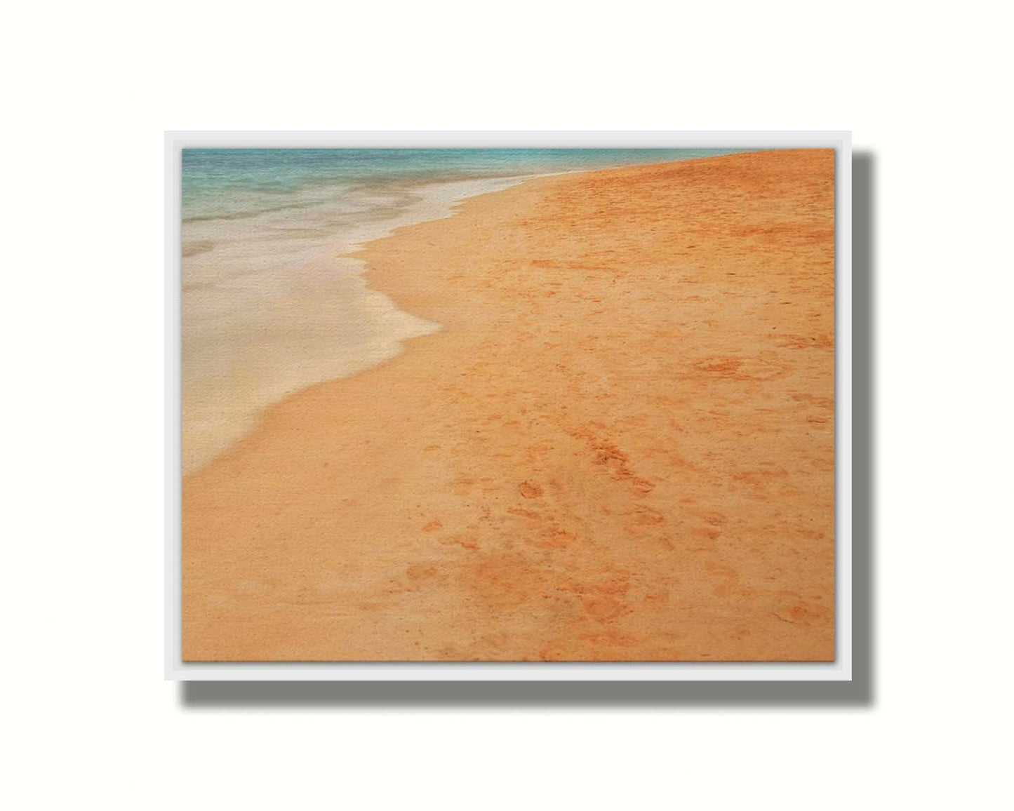 A photograph of beach sand. The warm hues of golden sand are contrasted by the cool ocean water. Printed on canvas in a float frame.