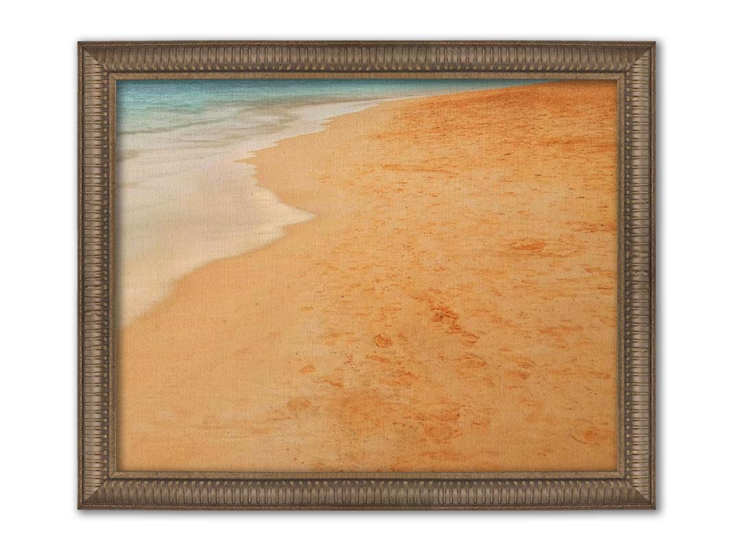 A photograph of beach sand. The warm hues of golden sand are contrasted by the cool ocean water. Printed on canvas and framed.