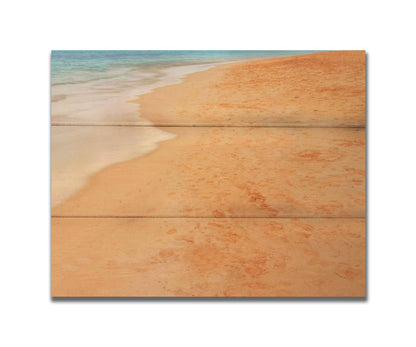 A photograph of beach sand. The warm hues of golden sand are contrasted by the cool ocean water. Printed on a box board.