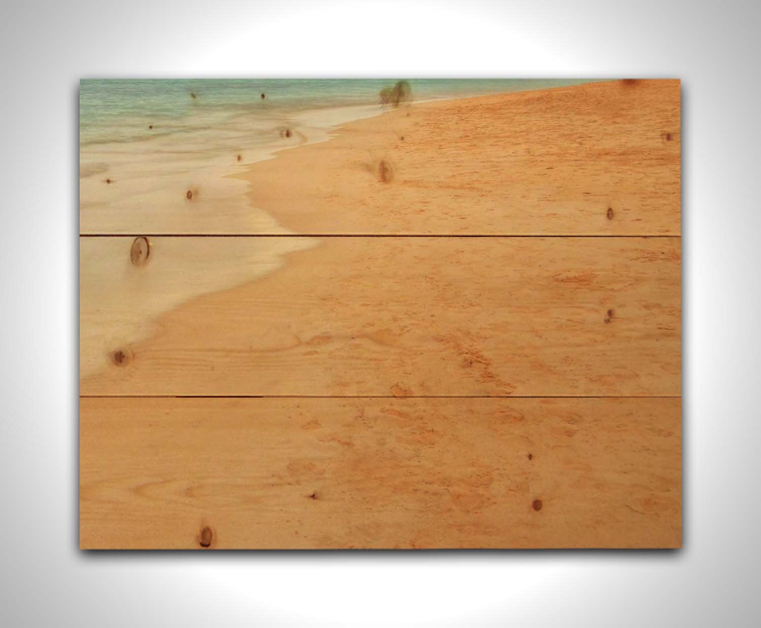 A photograph of beach sand. The warm hues of golden sand are contrasted by the cool ocean water. Printed on a wood pallet.