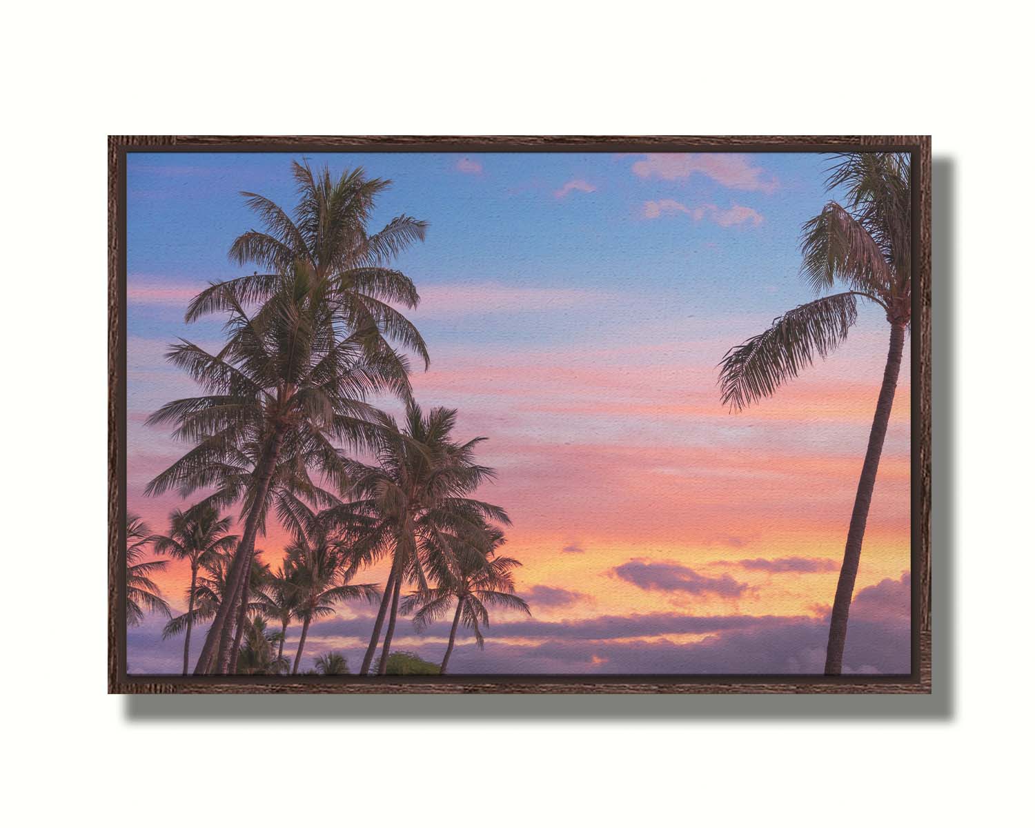 A photograph of Hawaiʻian palm trees, backed by a sunset sky in orange, pink, and blue. Printed on canvas in a float frame.