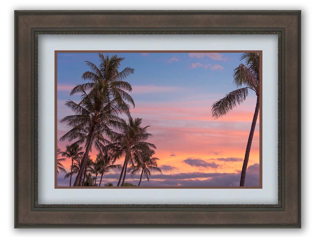 A photograph of Hawaiʻian palm trees, backed by a sunset sky in orange, pink, and blue. Printed on paper, matted, and framed.