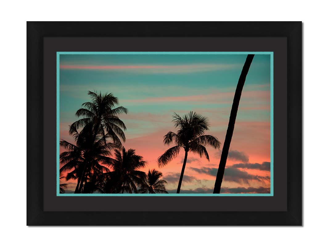 A photograph of Hawaiʻian palm trees, sihouetted against a sunset sky in orange, pink, and blue. Printed on paper, matted, and framed.