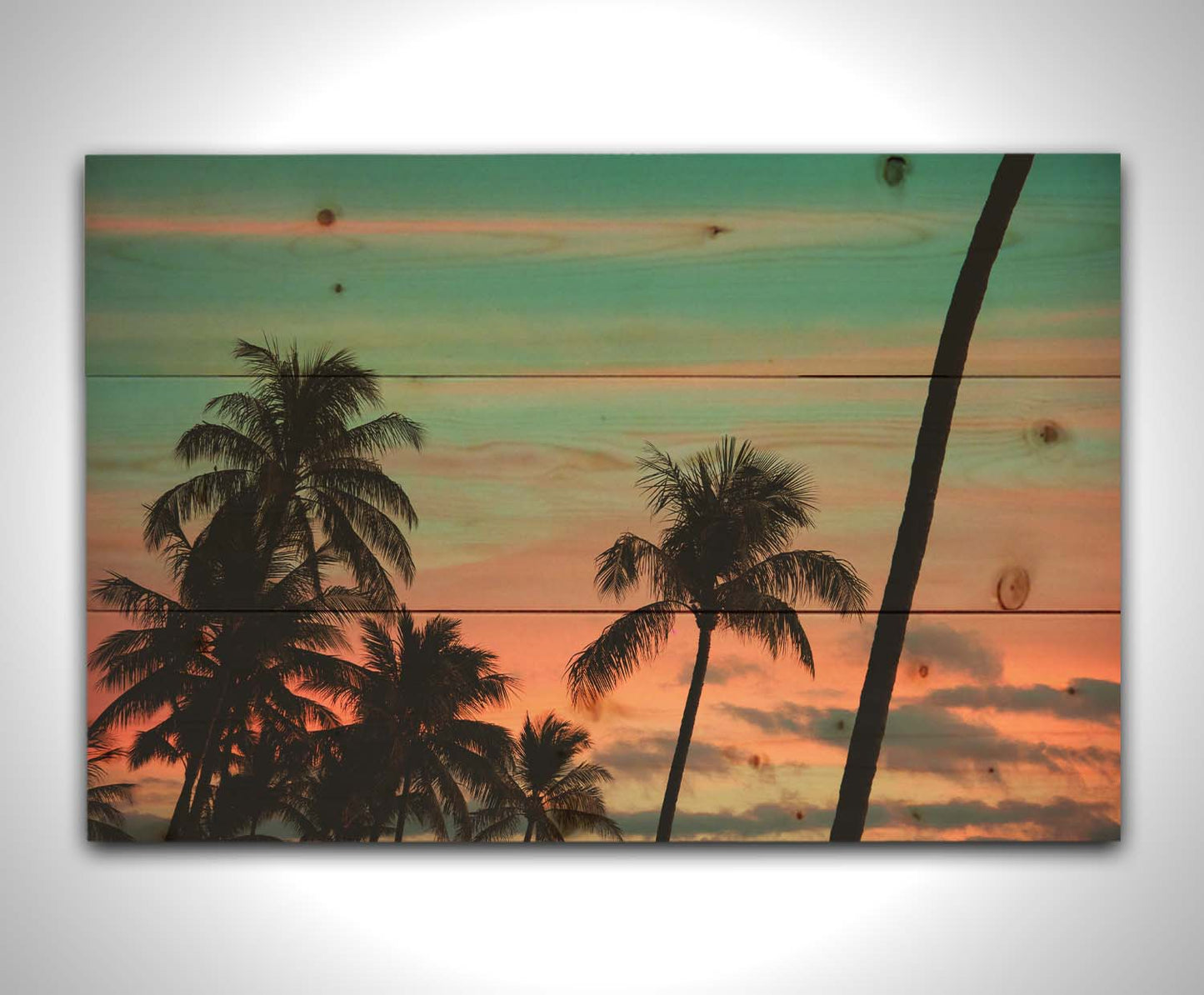 A photograph of Hawaiʻian palm trees, sihouetted against a sunset sky in orange, pink, and blue. Printed on a wood pallet.