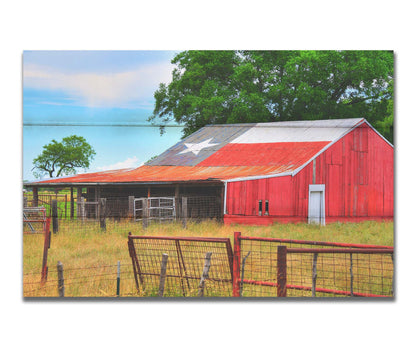 A photograph of a red barn, with a Texas flag painted on the roof. It is surrounded by red ranch fences and grassy fields. Printed on a box board.