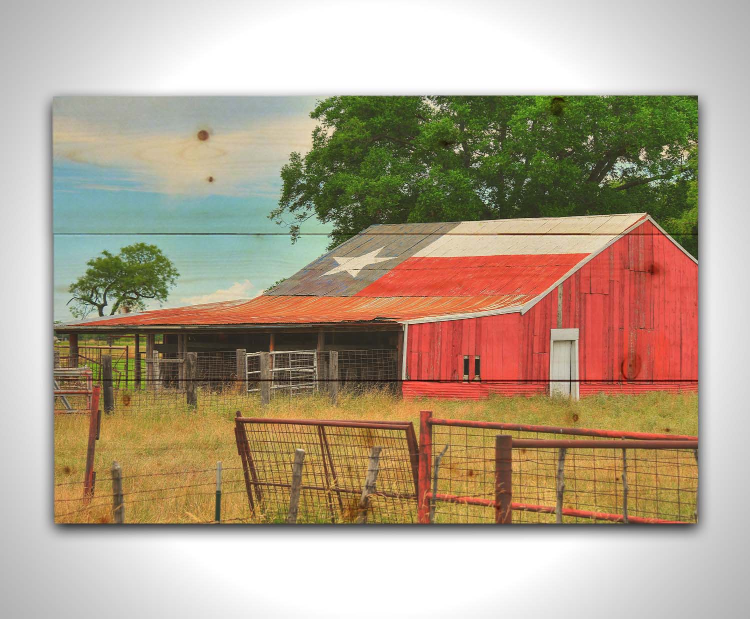 A photograph of a red barn, with a Texas flag painted on the roof. It is surrounded by red ranch fences and grassy fields. Printed on a wood pallet.