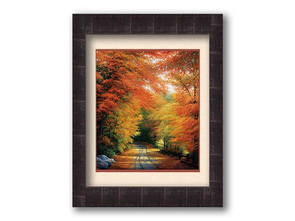 A painting of a road winding through a forest during fall. The red, orange, and yellow leaves shed to the ground, lining the road. Printed on paper, matted, and framed.