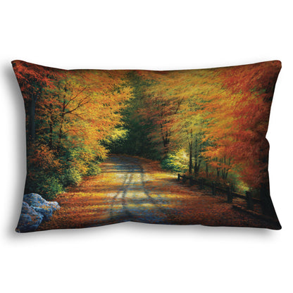 Decorative pillow with a painted autumn forest design. Red, orange, and yellow trees line a road winding through the forest.