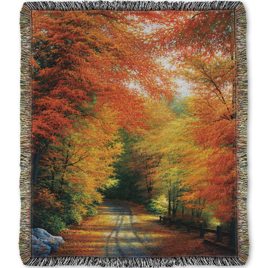 Woven throw blanket with a painted autumn forest design. Red, orange, and yellow trees line a road winding through the forest.