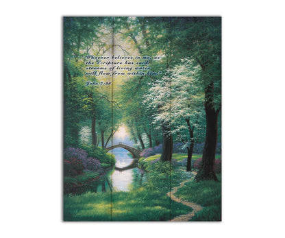 A painting of a stream through a lush green forest trail, with a bridge crossing in the distance. Printed on a wood pallet.