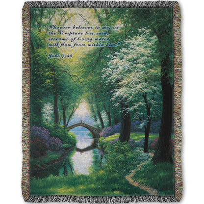 Woven throw blanket designed with a painting of a stream through a lush green forest trail, with a bridge crossing in the distance.