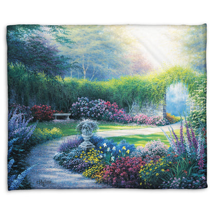 A coral fleece blanket designed with a painting of a serene path through a garden filled with bushes of flowers bathed in a gentle light.
