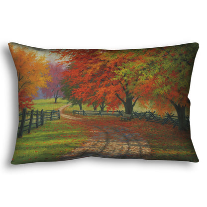 A throw pillow designed with a painting of a road winding through a fenced field, surrounded by multicolored fall maple trees.