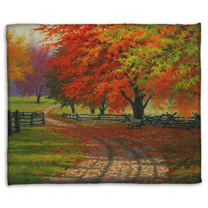 A fleece throw blanket designed with a painting of a road winding through a fenced field, surrounded by multicolored fall maple trees.