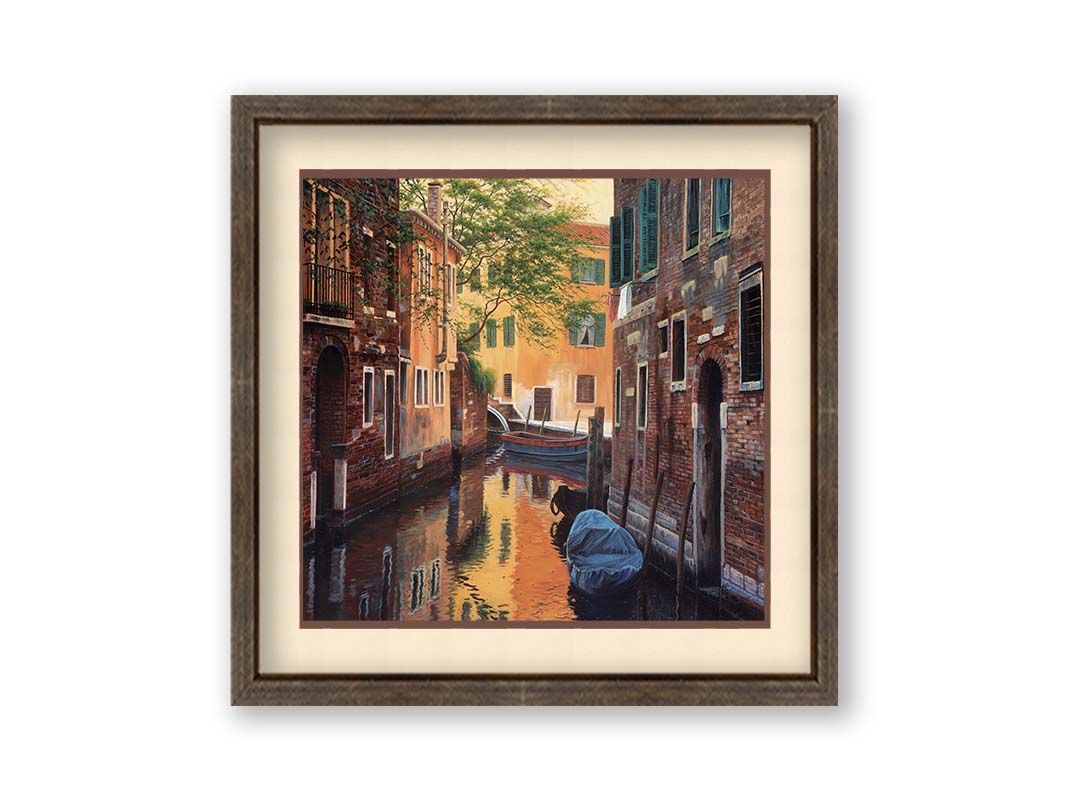 A painting of a canal alleyway between old brick buildings in Venice, Italy, during the day. The buildings reflect off the water in which a few small wood boats float. Printed on paper, matted, and framed.