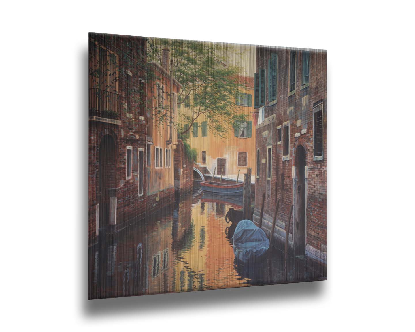 A painting of a canal alleyway between old brick buildings in Venice, Italy, during the day. The buildings reflect off the water in which a few small wood boats float. Printed on metal.