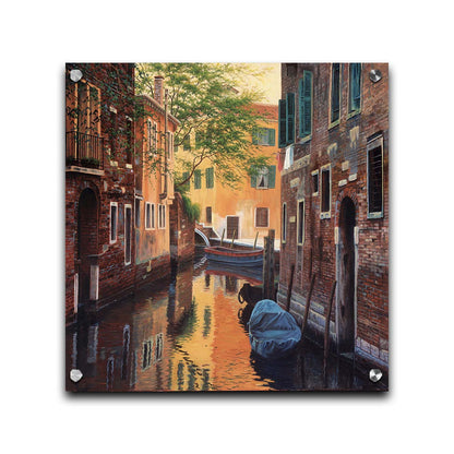 A painting of a canal alleyway between old brick buildings in Venice, Italy, during the day. The buildings reflect off the water in which a few small wood boats float. Printed on acrylic.