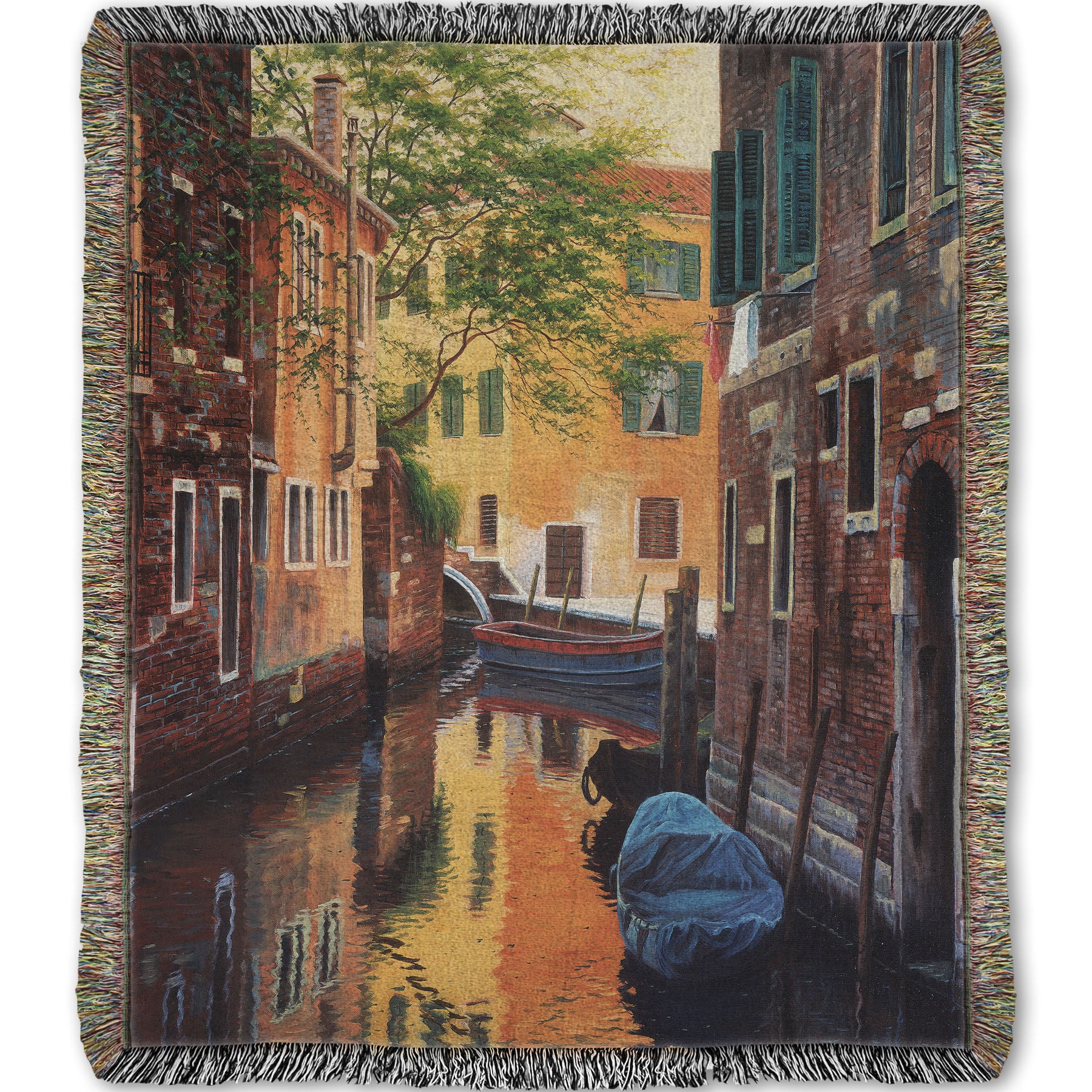 A woven throw blanket designed with a painting of a canal alleyway between old brick buildings in Venice, Italy, during the day. The buildings reflect off the water in which a few small wood boats float.