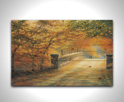 A painting looking down a bridge road during fall. The trees lining the road have turned yellow and orange for autumn, and some of their fallen leaves are scatted along the path. Printed on a wood pallet.