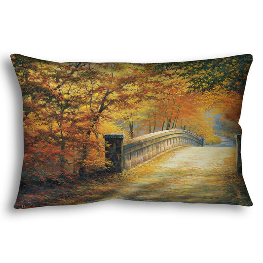 A throw pillow designed with a painting looking down a bridge road during fall. The trees lining the road have turned yellow and orange for autumn, and some of their fallen leaves are scatted along the path.