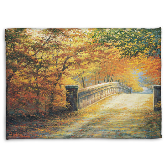 A fleece blanket designed with a painting looking down a bridge road during fall. The trees lining the road have turned yellow and orange for autumn, and some of their fallen leaves are scatted along the path.