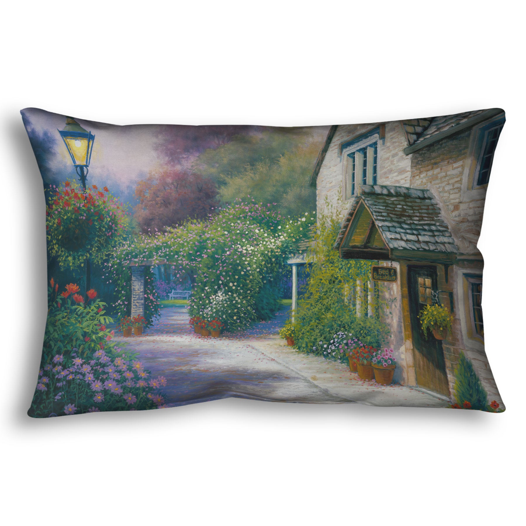 A throw pillow designed with a painting of a bed and breakfast storefront, with a streetlamp-lined path leading to the garden full of blooming flowers.