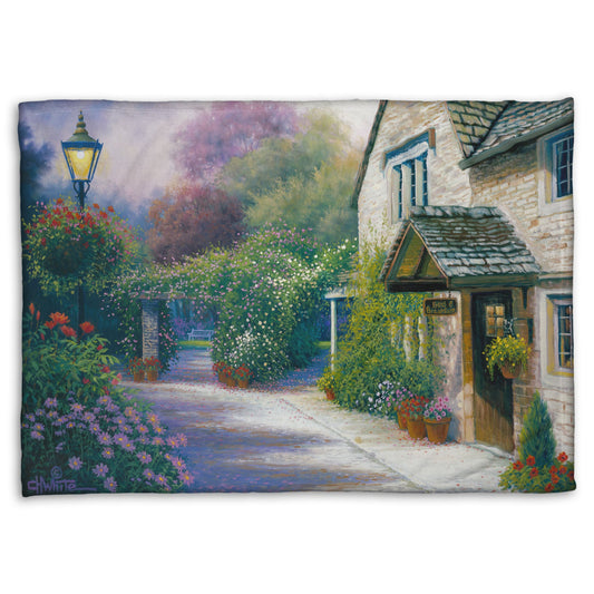 A fleece throw blanket designed with a painting of a bed and breakfast storefront, with a streetlamp-lined path leading to the garden full of blooming flowers.