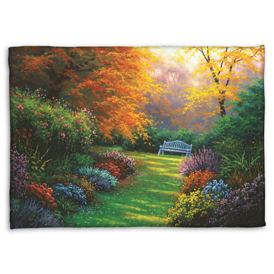 A fleece throw blanket designed with a painting of a garden path during fall. The trees surrounding the garden have turned orange and yellow. A grassy path through the garden is surrounded by bushes of flowers in every color, and a bench can be seen up ahead.