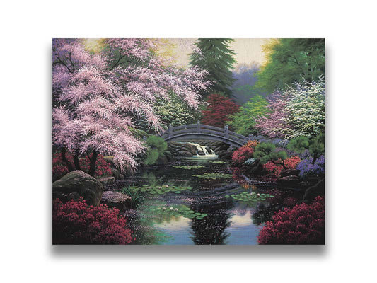 A painting of a tranquil pond surrounded by pink, red, and green flowered trees and shrubs. Lilly pads and fallen pink blossoms float on the water, which is crossed by a wooden bridge. Printed on canvas.