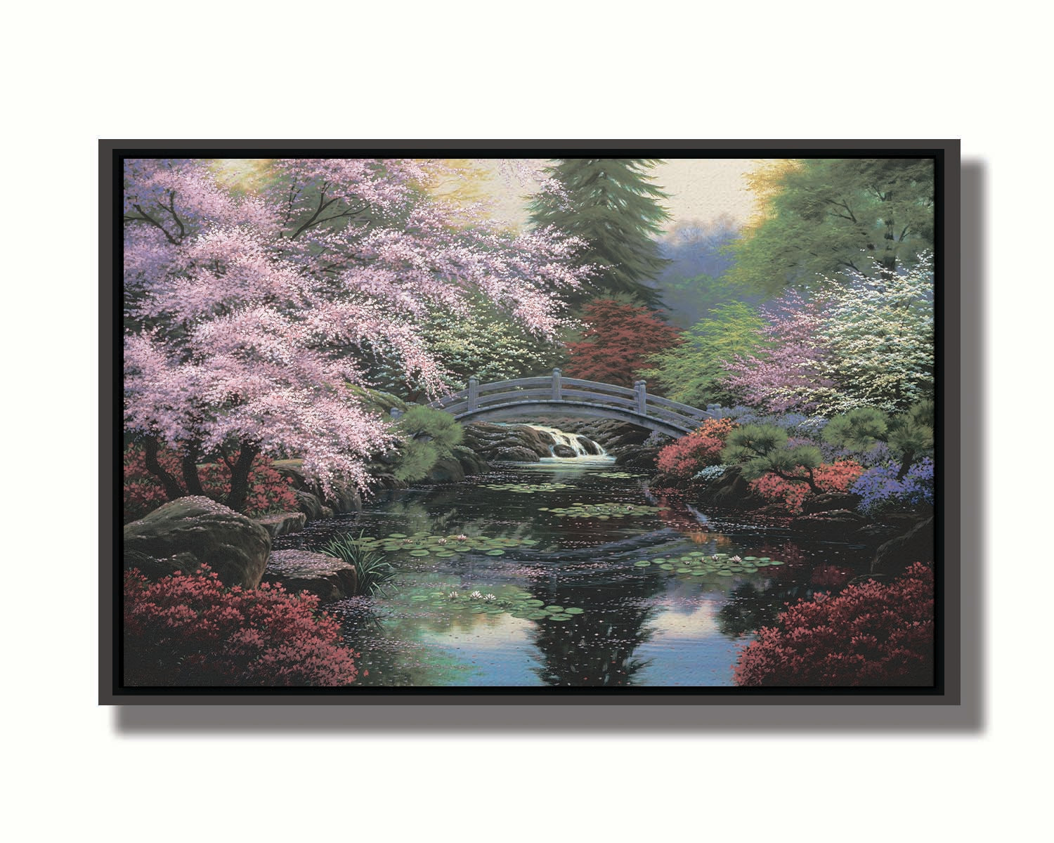 A painting of a tranquil pond surrounded by pink, red, and green flowered trees and shrubs. Lilly pads and fallen pink blossoms float on the water, which is crossed by a wooden bridge. Printed on canvas in a float frame.