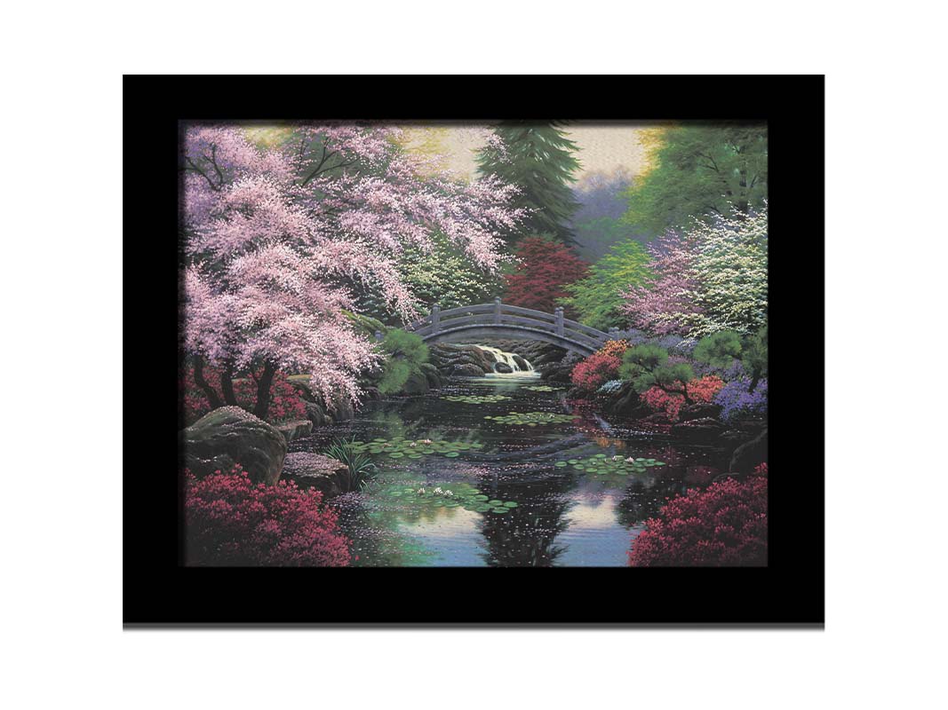 A painting of a tranquil pond surrounded by pink, red, and green flowered trees and shrubs. Lilly pads and fallen pink blossoms float on the water, which is crossed by a wooden bridge. Printed on canvas and framed.