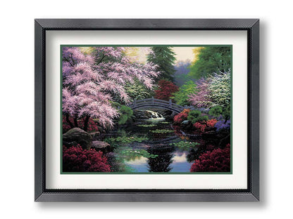 A painting of a tranquil pond surrounded by pink, red, and green flowered trees and shrubs. Lilly pads and fallen pink blossoms float on the water, which is crossed by a wooden bridge. Printed on paper, matted, and framed.