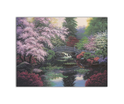 A painting of a tranquil pond surrounded by pink, red, and green flowered trees and shrubs. Lilly pads and fallen pink blossoms float on the water, which is crossed by a wooden bridge. Printed on a box board.