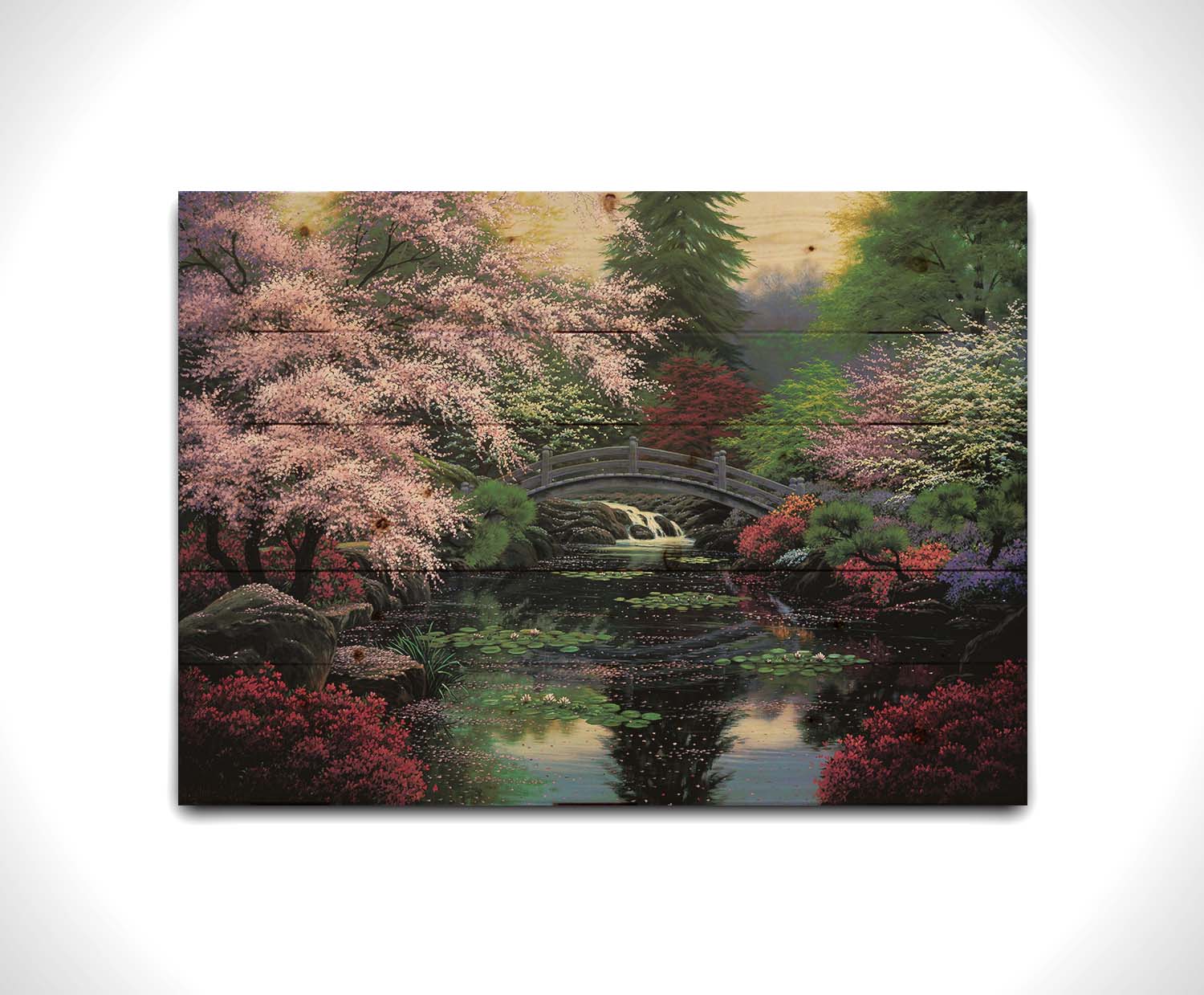 A painting of a tranquil pond surrounded by pink, red, and green flowered trees and shrubs. Lilly pads and fallen pink blossoms float on the water, which is crossed by a wooden bridge. Printed on a wood pallet.