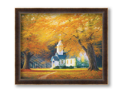 A painting of a white church in a forest of yellow and orange trees. Deer roam in the leaf-coated yard, and sun beams shine through the trees to highlight the building. Printed on canvas and framed.