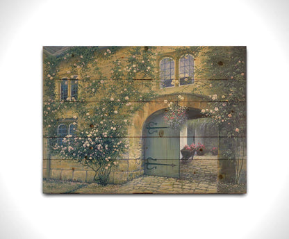 A painting of an arched doorway passing through a building into a courtyard. The building and courtyard are decorated with bushes and vines sprouting an assortment of white and red flowers. Printed on a wood pallet.