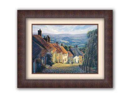 A painting looking down a cobblestone road on a hill lined with houses. A person can be seen walking down the path past flower-laden walls. Printed on paper, matted, and framed.