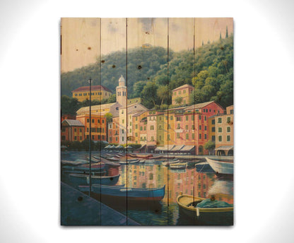 A painting of the colorful fishing town of Portofino. Many small boats are docked in the waters in the foreground, and the steep hills in the background are lush with trees. Printed on a wood pallet.